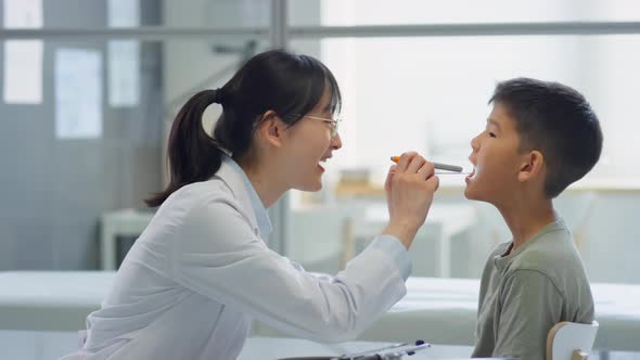 Female Doctor Examining Throat of Asian Tween Boy alt