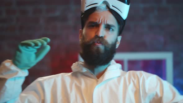 Happy Hipster Man in Covid19 Protective Suit and Gloves Dancing Indoors alt