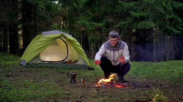 A Man Warms His Hands Over a Fire in the Forest alt