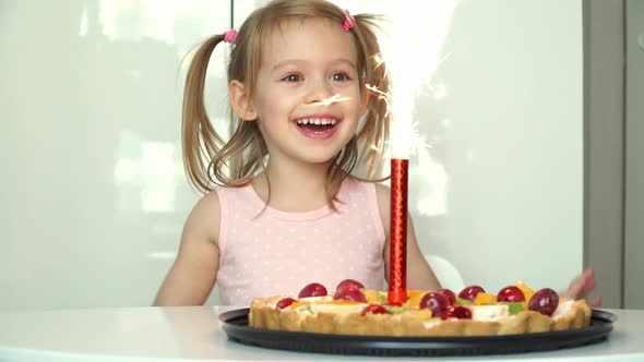 Little Girl Laughs Smiles and Looks at Burning Fireworks in Cake