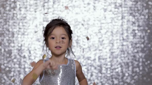 Cute Happy Little Girl Child in a Silver Dress Dancing on Background of Silver Bokeh.