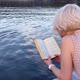 A Blonde with Short Hair Reads a Book Against the Background of a Lake - VideoHive Item for Sale
