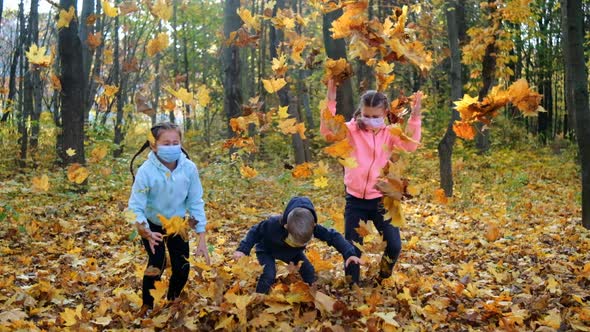 Small children in medical masks throw fallen yellow leaves in the Park on an autumn day