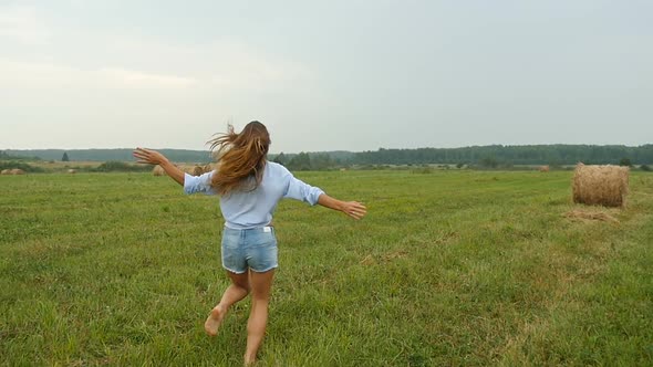 Rear View of Happy Young Woman Running on Grass Field With Haystacks