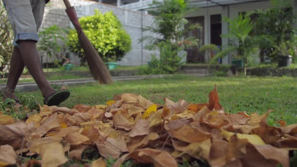 Young Man in Flip Flops Holds Broom and Cleans Leaves alt