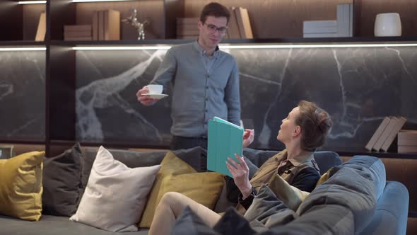 Positive Woman Sitting in Furniture Showroom Choosing Furnishings and Decorations As Man Bringing alt