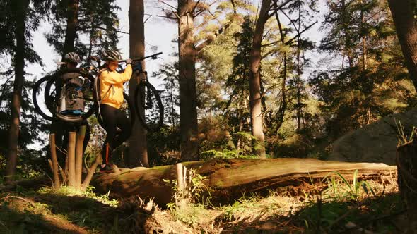 Mountain biking couple carrying bicycle while walking on a log alt