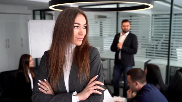 Young Charming Businesswoman Is Watching at Camera in Office, Smiling, Her Colleagues Are Networking