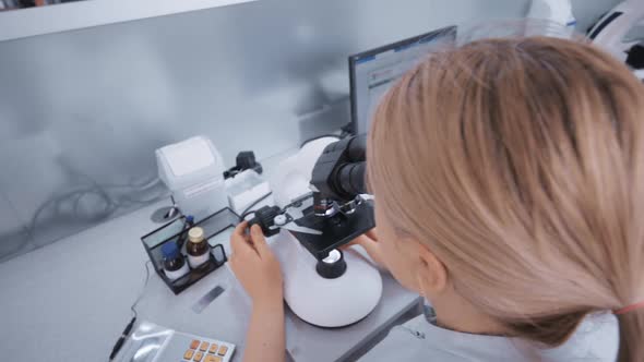 a Doctor in a Modern Clinic Works Behind a Fluorescent Led Microscope alt
