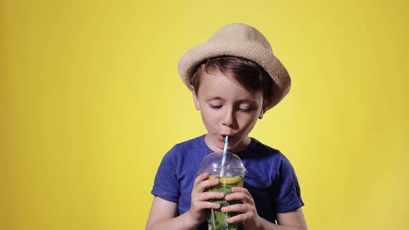 Cute boy Drinking Mojito cocktail From Plastic Cup Over Yellow Studio Backgroun alt