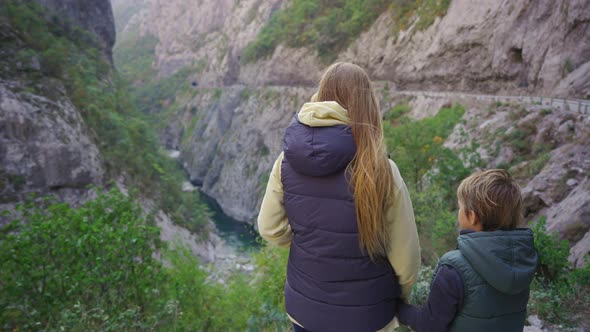 A Woman and Her Son Stand at the Roadside Observing a Magnificent Canyon of the Moracha River alt