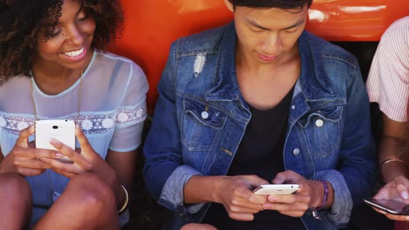Friends using mobile phone near camper van in park alt