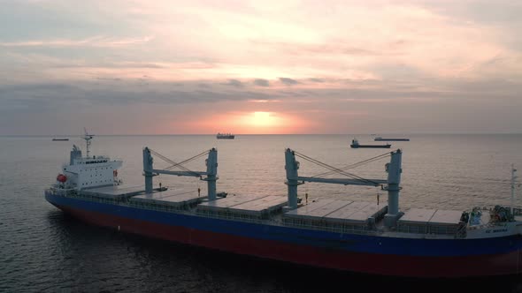 A drone flight around container ships into the sea at sunrise alt