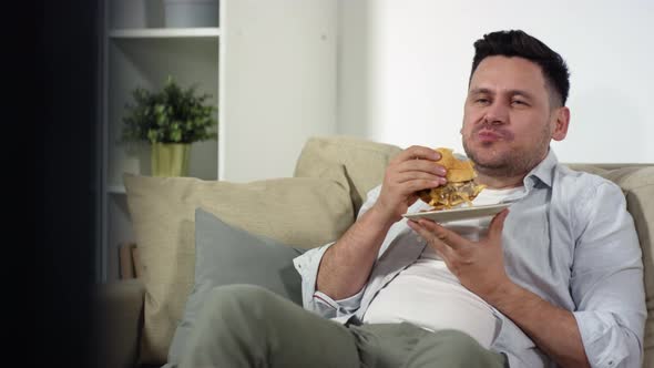 Middle Aged Single Man Eating Burger and Watching TV at Home alt