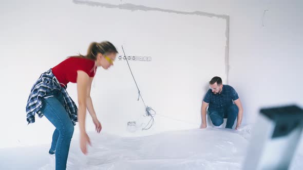 Couple Covers Floor with Foil Near White Wall in Own House alt