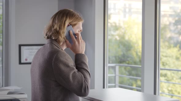 Businessman Calling By Smartphone While Standing By Office Window alt