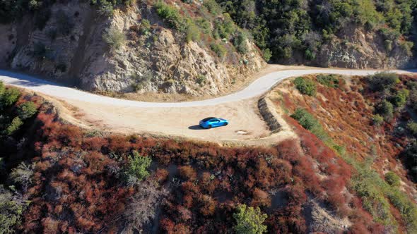 Slow drone shot flying around a blue Tesla Model S on a small mountain road on Mt. Baldy in SoCal. alt