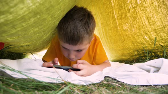 Child Reading Ebook on Mobile Outdoor. Kid with Gadget in Park, Garden. Boy in Cap Playing Game on