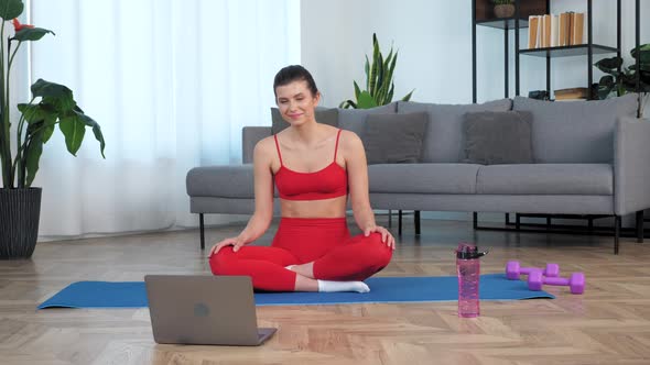 Smiling Fit Woman Sits on Yoga Mat Watch Distance Sport Education Lesson Course alt