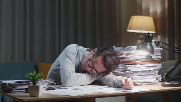 Tired Asian Man Yawning And Sleeping While Working Hard With Documents At Home alt