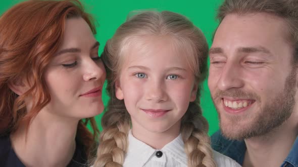 Happy Family Charming Woman and Joyful Man Kiss Beautiful Girl on Cheek Smiles and Looks at Camera alt