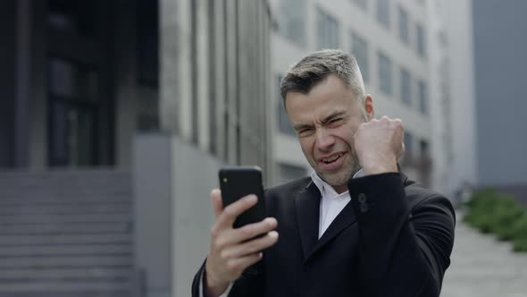 Crop View of Happy Mature Man in Classical Suit Rejoicing and Looking at Smartphone Screen alt
