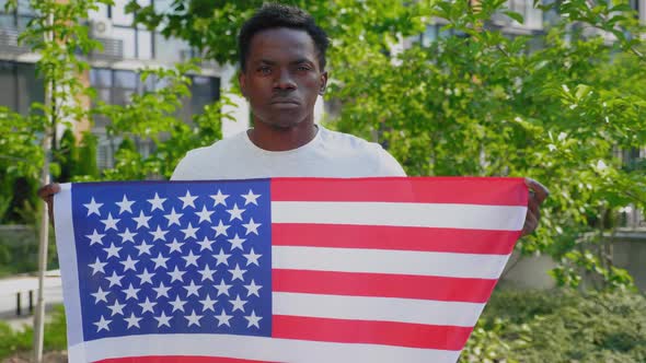 Portrait Afroamerican Man Holding an American Flag and Looks Camera in Summer alt