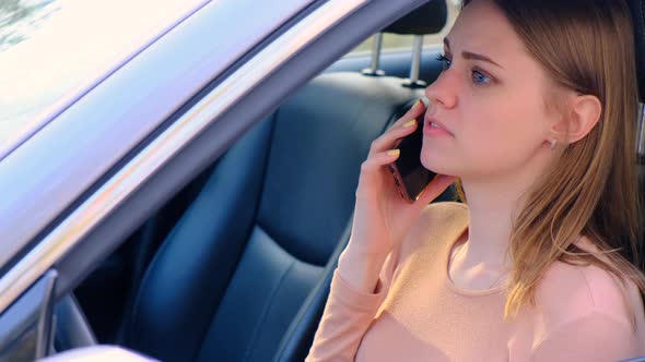 Young Upset Woman is Talking on the Phone While Driving a Standing Car