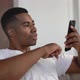 Closeup Face of Focused AfricanAmerican Man in Tshirt Sitting at Armchair Using Mobile Phone