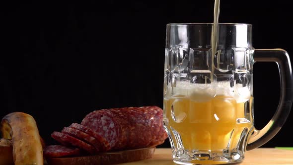 Pouring beer into the glass. Sausage with mug cold craft beer in a glass with water drops alt