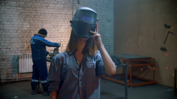Young Sexy Woman Standing in the Workshop and Putting on a Helmet Holding an Angle Grinder alt