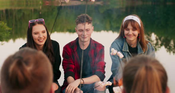 A Group of Happy Young Adults Roasts Marshmallows Over a Campfire Outdoors alt