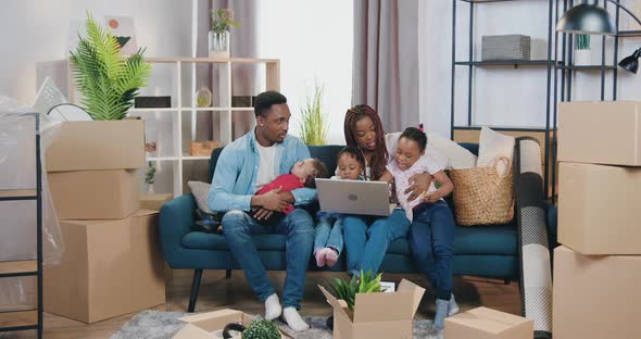 Mother Sitting on the Sofa Together with Her Two Small Daughters and Using Laptop while Her husband alt