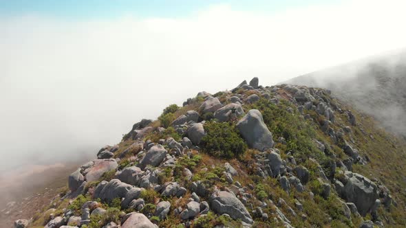 Man stands on mountain peak as drone flies 360 above him through the clouds