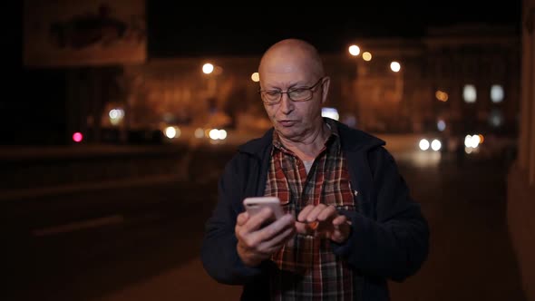 An Elderly Man with a Night on the Road Use a Smartphone