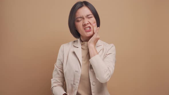 Asian business woman was sick with tooth ache and standing isolated over beige background. 4K video