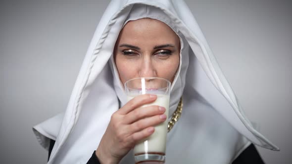 Closeup of Woman in Nun Costume Enjoying Taste of Milk Licking Lips Looking at Camera Smiling alt