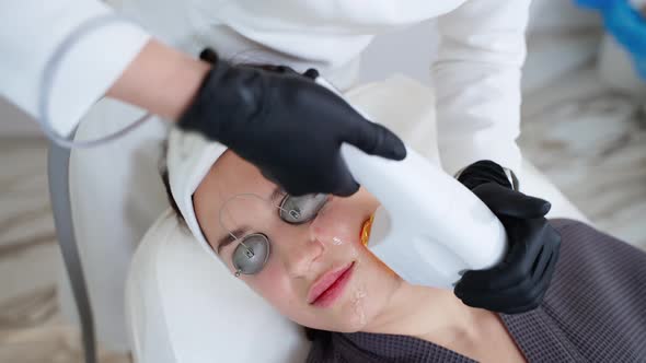 Aesthetic Procedure in Modern Cosmetology Clinic Expert Beautician is Using Phototherapy Apparatus alt