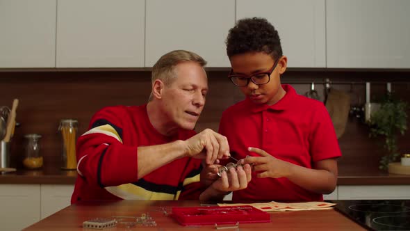 Grandpa and School Age Black Grandson Assembling Toy From Metallic Constructor alt