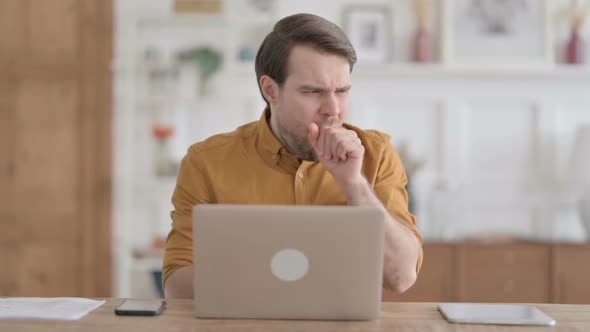 Young Man Coughing while using Laptop in Office alt