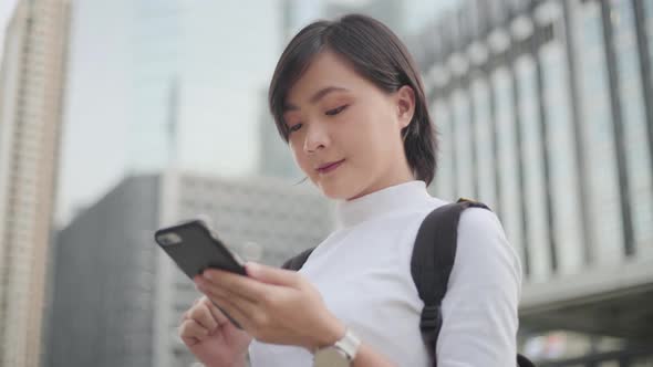 Happy asian woman walks down the city street and use smartphone. Positive emotion