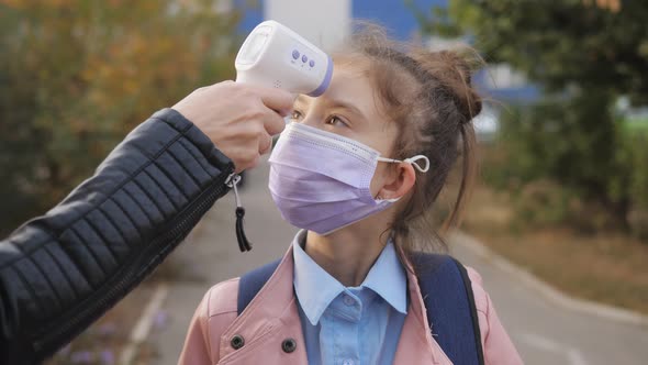 Closeup of a Schoolgirl's Temperature Measurement Using an Electronic Thermometer in Front of School alt
