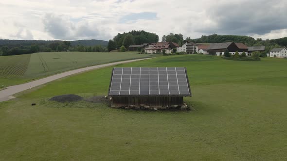 Sheep graze on a field near a barn with solar panels alt
