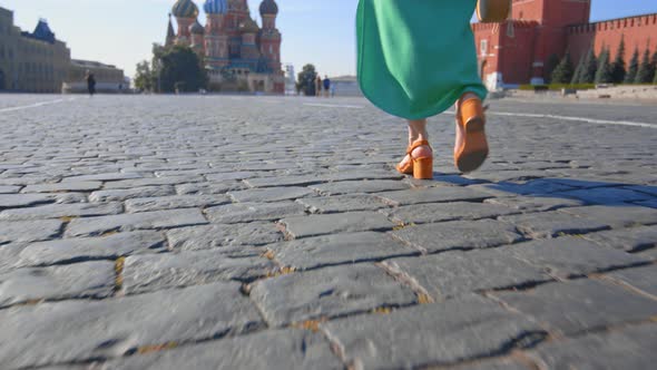 A girl in a green dress walking along the sett in Red Square alt