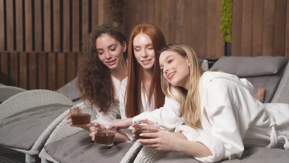 Three Young Ladies Clothed Bathrobe Lying on Deckchairs Talking and Drinking Tea