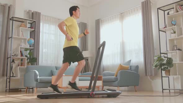 Side View Of Asian Man Running On A Treadmill At Home alt