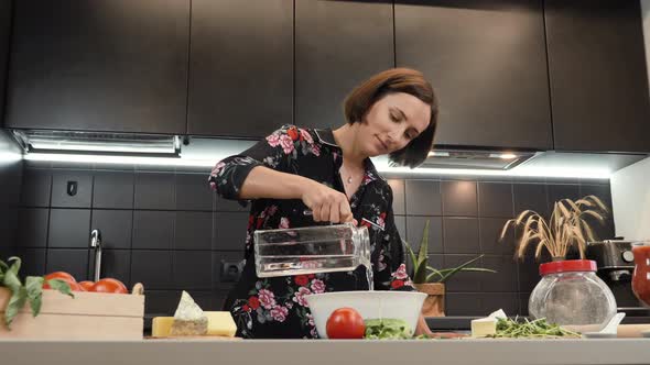 Woman cooking dough for pizza at home kitchen. Female adding water to flour alt
