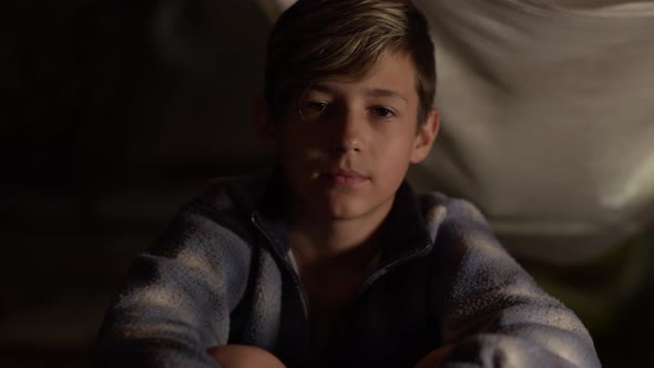 Serious Bully Boy Sitting Indoors Looks Up and Looking at the Camera