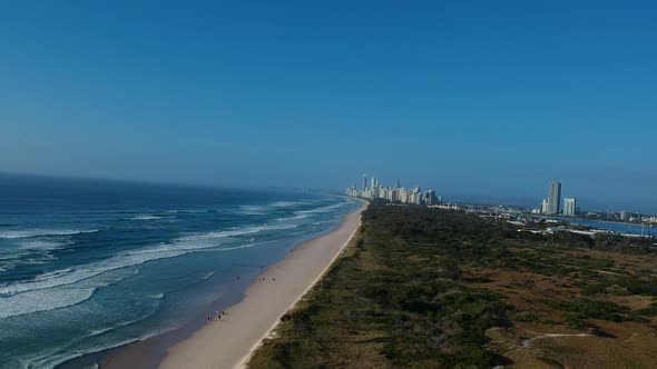 Aerial view of a popular beach near a large area of green space with a sprawling city skyline in the alt