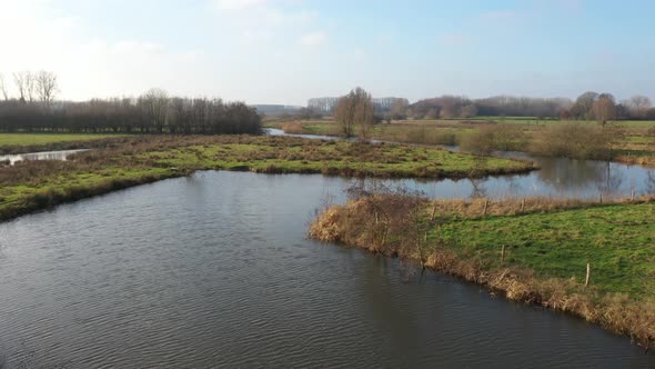 A river that is meandering through bright green colored grass of the surrouding meadows in europe